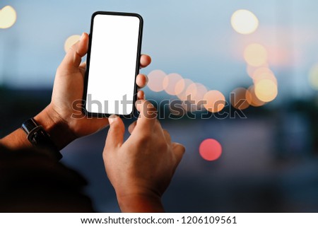 Male hand holding blank screen mobile smart phone at street night.