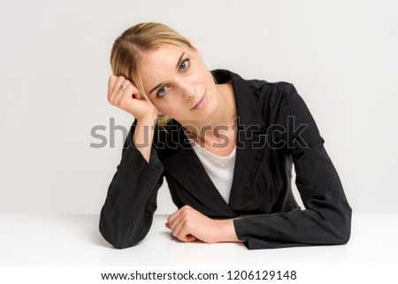 Studio photo of a beautiful blonde girl talking in a business suit on a white background sitting at the table. She is sitting right in front of the camera, smiling and looking happy.