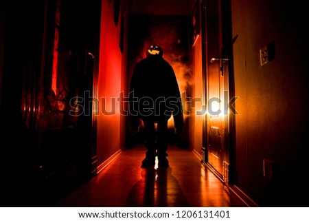 Halloween concept. Creepy silhouette in the dark corridor with pumpkin head. Toned light with fog on background.