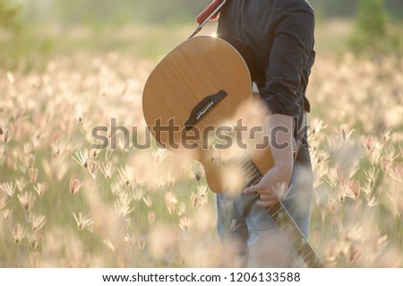 Detail of a man playing guitar,musician playing acoustic guitar,concept for sunset over a misty meadow in summer evening and Flower nature dry field on sun background.