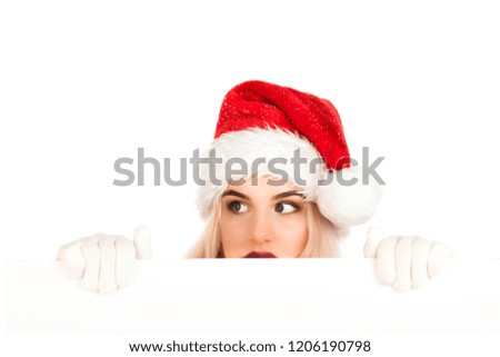 Attractive smiling young girl dressed in Santa's hat holds flipchart board and dreams about gifts. Christmas and New Year advertising concept isolated on blurred white background with blank copy space