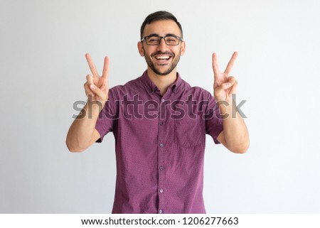 Happy professional gesturing peace. Young man in glasses and casual maroon shirt showing victory signs with both hands. Gesturing and achievement concept