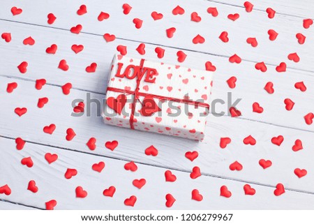 Valentines day concept with hearts and gift box. gift box with a red heart on a white wooden table. Present box with red ribbon. Small hearts flying over it.