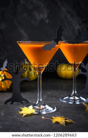 Orange martini cocktails with bats and decor for Halloween party, on dark background