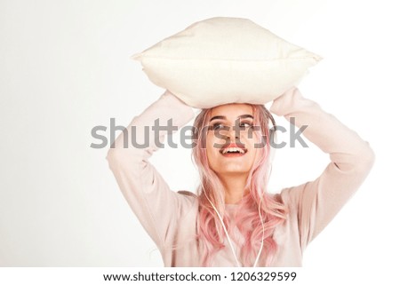 Young attractive smiling girl dressed in sleeping suit hugs the pillow and listening the music by headphones dreams about gifts. Christmas, New Year advertising. Isolated on blurred white background