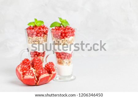 Pomegranate parfait - sweet organic layered dessert with granola flakes, yogurt and ripe fruit seeds in beautiful glasses on gray background with copy space. Natural vegetarian healthy food.