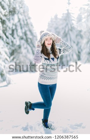 Beautiful happy laughing young woman wearing winter hat gloves and scarf covered with snow flakes. Winter forest landscape background
