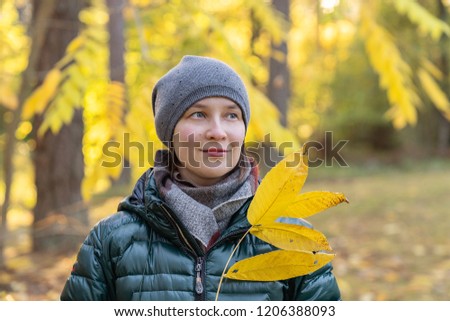 young woman is holding yellow walnut autumn leaves in a park