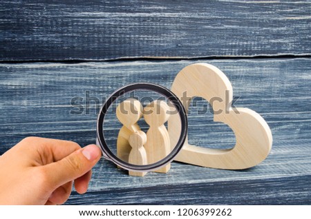 Magnifying glass is looking at the young family with a child is standing near a wooden heart. Love and loyalty, a strong young family. Family relationships. Civil marriage. Extramarital children.