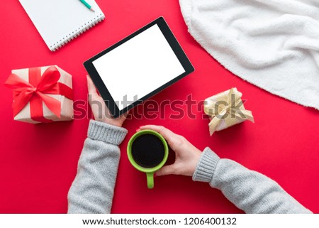 Female hands, woman holding a tablet pc and Cup of coffee or tea. Red table, gifts boxes for the holidays, background with copy space for advertisement, top view