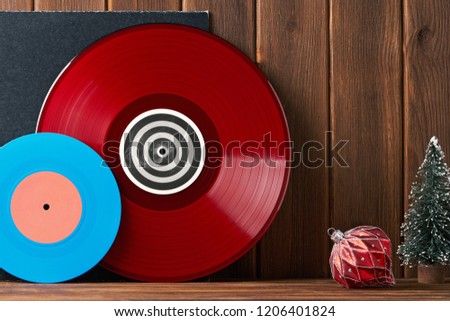 Christmas greeting card frame. Bright red and blue vinyl records for turntable on gray carpet and red glass vintage ball, Christmas tree on an old wooden plank. Front view. Noel
