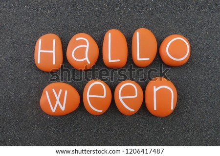 Halloween text composed with orange painted stones over natural black volcanic sand