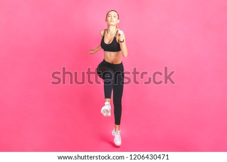 Young beautiful woman with fit body jumping and running isolated over pink background. Female model in sportswear exercising.