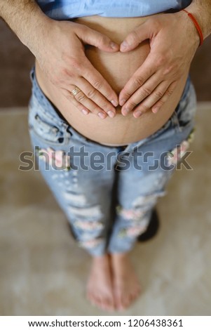 Heart-shaped mother and father's hands on the pregnant belly.