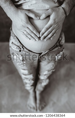 Heart-shaped mother and father's hands on the pregnant belly. Black and white picture.