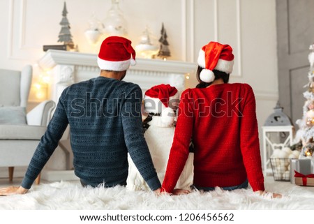New Year. Christmas. Family. Back view of young parents and their little daughter in Santa hats spending time together at home