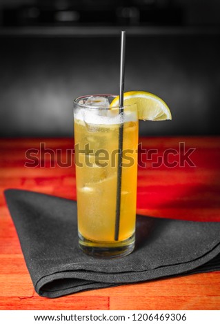 A yellow cocktail with a lemon garnish on a black cloth napkin on a red wooden table.