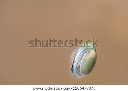 Closeup of silver metallic push button switch used to turn on power to machine on soft brown background. 