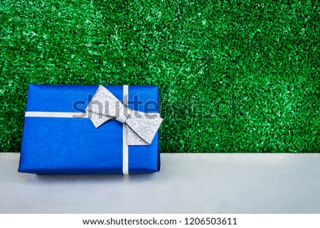 Blue gift box and silver bow on green background for New Year's Eve, Christmas and special occasion.