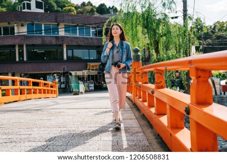 full length photo of an elegant asian traveler walking on the bridge with an attractive smile on her face. Famous sightseeing Uji bridge in Kyoto. lady travel photographer lifestyle.