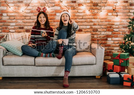 friends watching comedy at home on christmas eve. young girl laughing pointing at the television. comfortable sitting on sofa in xmas holidays lifestyle.
