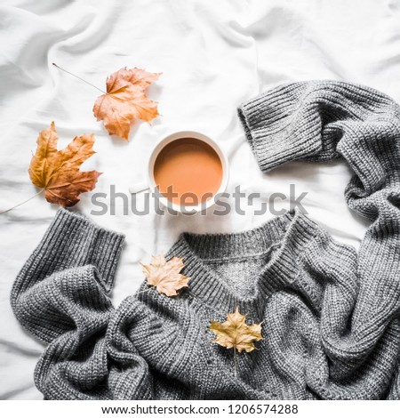 Cup of coffee, gray warm knitted sweater oversize, yellow dry leaves on the bed - cozy home still life, top view