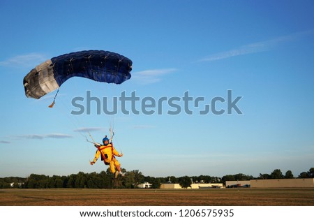 Skydiver under a dark blue little canopy of a parachute is landing on airfield, close-up. High-speed landing of a parachuter against the background of forests and buildings.  USA, Michigan