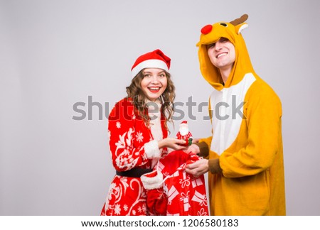 Christmas, celebration, people concept - Funny man in deer costume and woman in Santa Claus costume holding a Santa figurine in hands