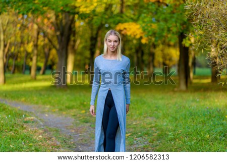 Photo portrait of a beautiful blonde girl in the park on the street in the fall in the sunset sun evening. She is standing in front of the camera, smiling and looking happy.