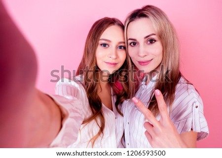 two beautiful and smiling female persons (mother and daughter) take photos selfie on the phone on a pink background in the studio. concept of love and family