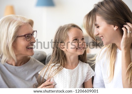 Smiling mother, daughter and grandmother sit on cozy couch at home having fun, three generations of women hugging enjoy spending time together, family of mom, granny and child relax indoors laughing Royalty-Free Stock Photo #1206609001