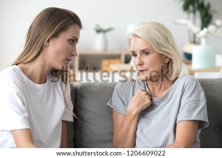 Concerned aged mother and adult daughter sit on couch having serious conversation, young woman talk with worried elderly mom, listen to her sharing problems or concerns, help dealing with depression Royalty-Free Stock Photo #1206609022