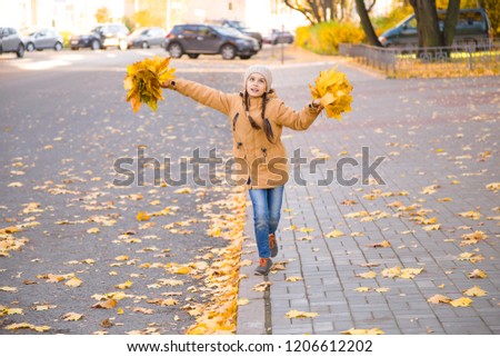 Happy little girl walking on the curb through the fallen maple leaves on a sidewalk in autumn city