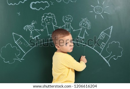 Little child drawing family with white chalk on blackboard