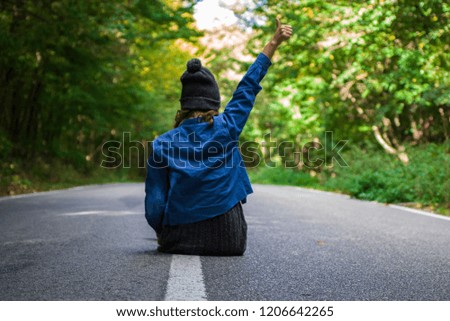 Girl sitting down on the road in the middle of the forest and showing ok sign