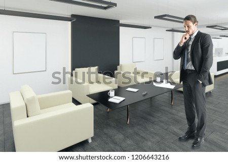 Thoughtful young european businessman standing in modern office lobby interior with posters. Mock up,