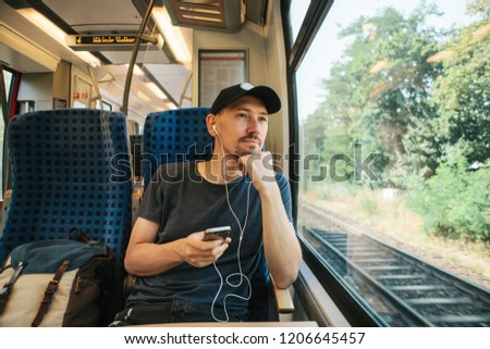 A young man listens to a music or podcast and looks out the window while the train is moving.