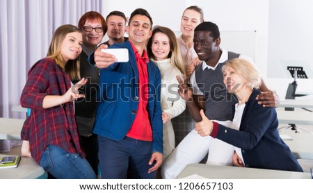 Friendly cheerful adult students of different nationalities making selfie in class