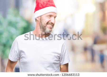 Middle age hoary senior man wearing christmas hat over isolated background looking away to side with smile on face, natural expression. Laughing confident.