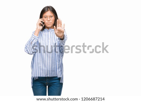 Young asian woman speaking on the phone over isolated background with open hand doing stop sign with serious and confident expression, defense gesture