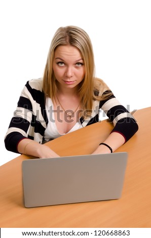 High angle view of a pretty young woman sitting at a wooden table working at her laptop looking up at the camera with a smile
