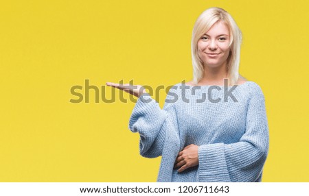 Young beautiful blonde woman wearing winter sweater over isolated background smiling cheerful presenting and pointing with palm of hand looking at the camera.