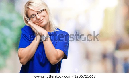 Young beautiful blonde woman wearing glasses over isolated background sleeping tired dreaming and posing with hands together while smiling with closed eyes.