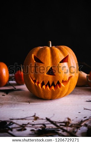 Jack o lanterns pumpkin with scary face on wooden table decorated with tree branches over black background. Spooky night. Halloween holiday concept. Party decoration