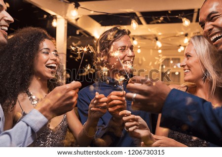 Friends celebrating christmas with bengal lights. Group of elegant women and men celebrating new year’s eve outdoor with sparklers. Smiling group of girls and guys with firework sticks outside. Royalty-Free Stock Photo #1206730315