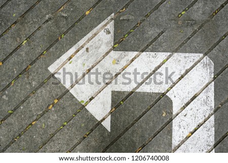 White painted road signage arrow on grey concrete pavement with fallen leaves for background and texture. (top view, space for text)