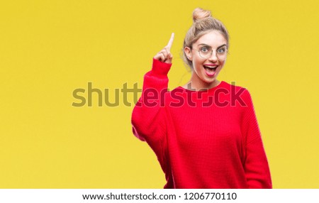 Young beautiful blonde woman wearing red sweater and glasses over isolated background pointing finger up with successful idea. Exited and happy. Number one.