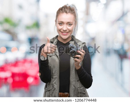 Young blonde woman taking pictures using vintage camera over isolated background happy with big smile doing ok sign, thumb up with fingers, excellent sign