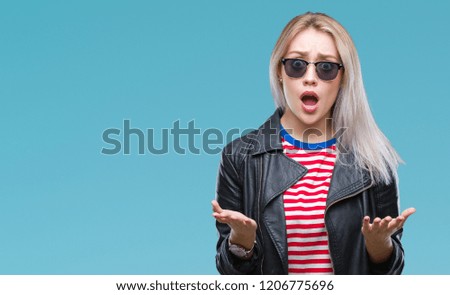 Young blonde woman wearing fashion jacket and sunglasses over isolated background afraid and shocked with surprise expression, fear and excited face.