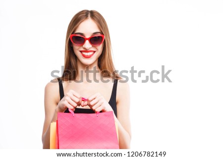 Gorgeous happy brunette woman wearing black dress and sunglasses holding shopping bags in front of herself on the white background, concept of consumerism, sale, rich life